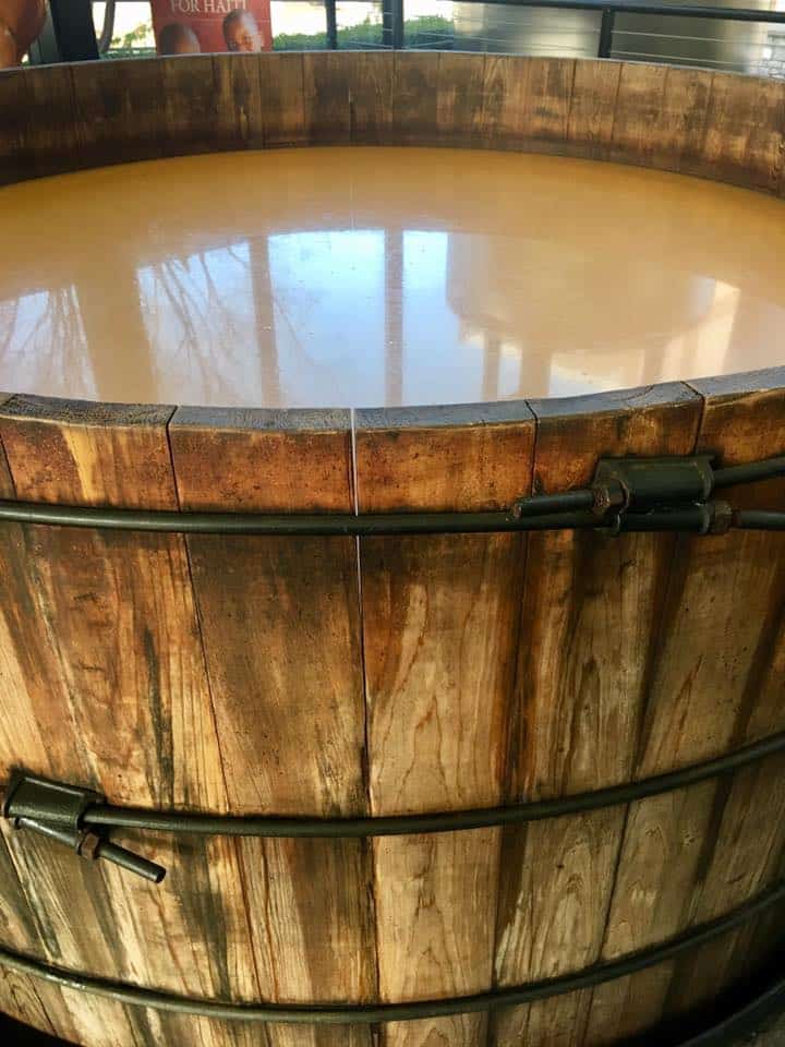 A close up image of a wooden barrel with a murky tan liquid inside. 