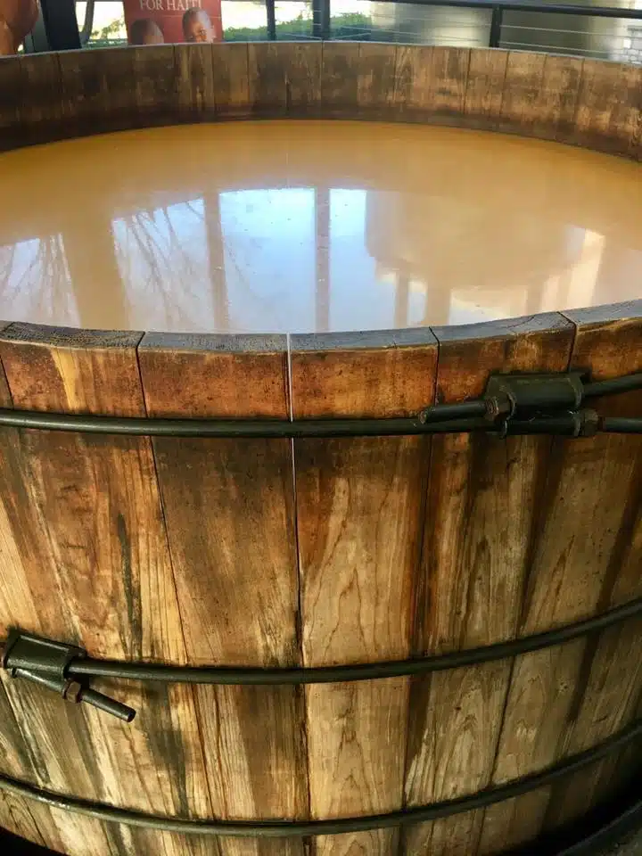 A close up image of a wooden barrel with a murky tan liquid inside.