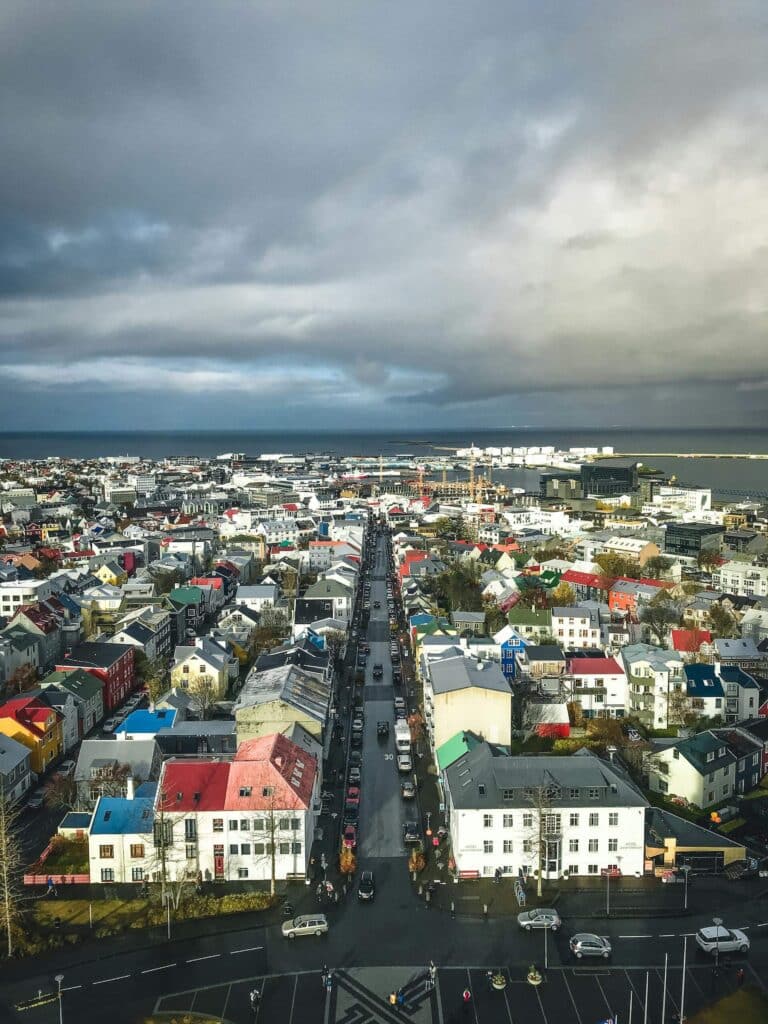 Aerial view of colorful buildings and roads in Reykjavík under a dramatic, cloudy sky.