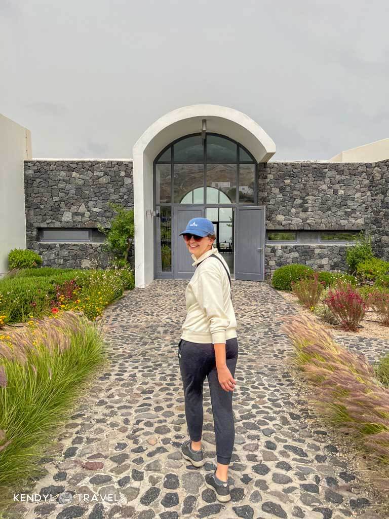 Traveler in casual clothes walking a cobblestone path toward a modern winery in Santorini