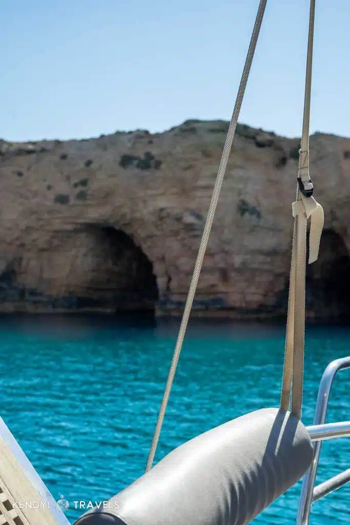 A view from the deck of a sailboat anchored near the sea caves of Naxos, with vibrant turquoise waters and rugged rock formations.