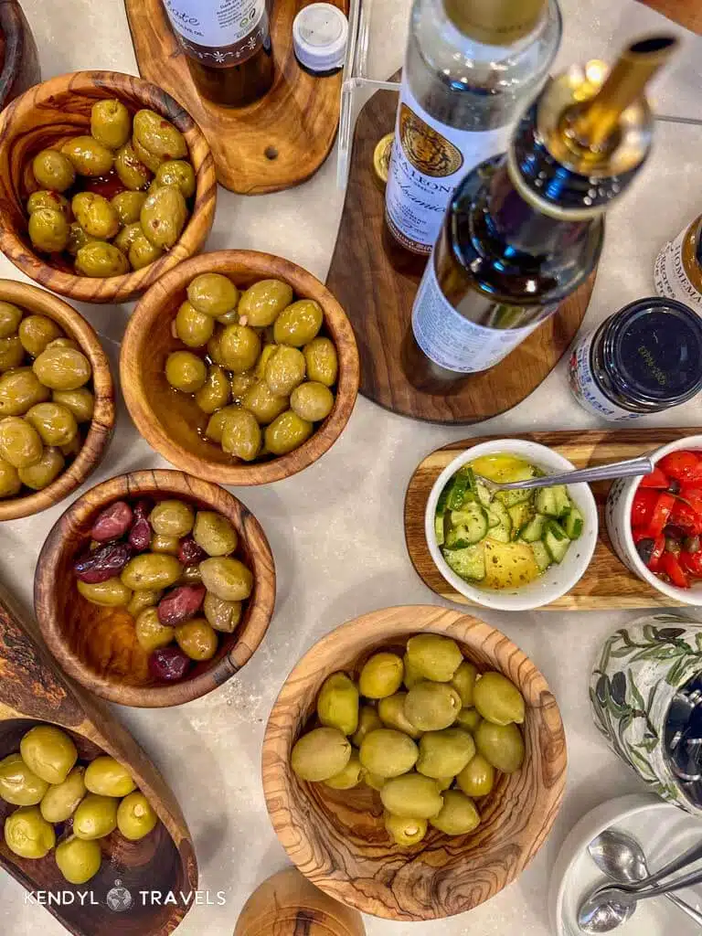 An overhead view of an olive oil tasting setup in Naxos, featuring assorted Greek olives, dipping oils, and fresh vegetables in wooden bowls.