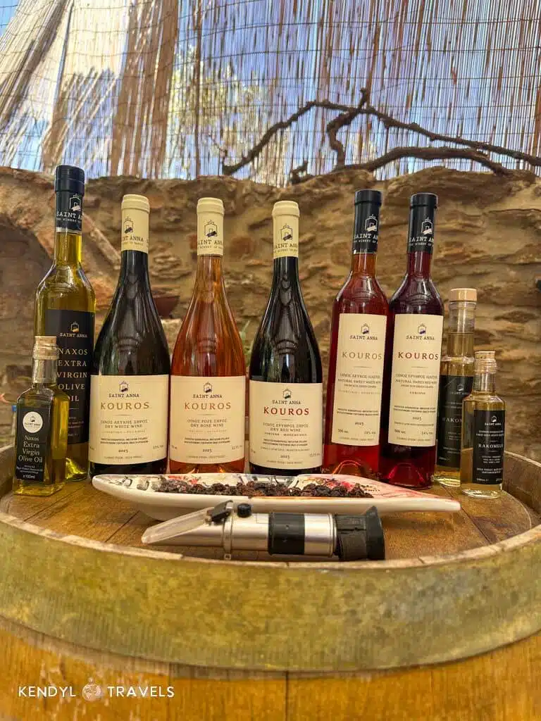 A rustic barrel-top display of Saint Anna wines and local olive oils, showcasing Naxos’ regional flavors and artisanal bottles.