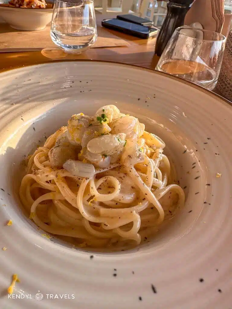 A close-up of a beautifully plated linguine dish with white sauce and shrimp, served at a cozy restaurant in Naxos during golden hour.