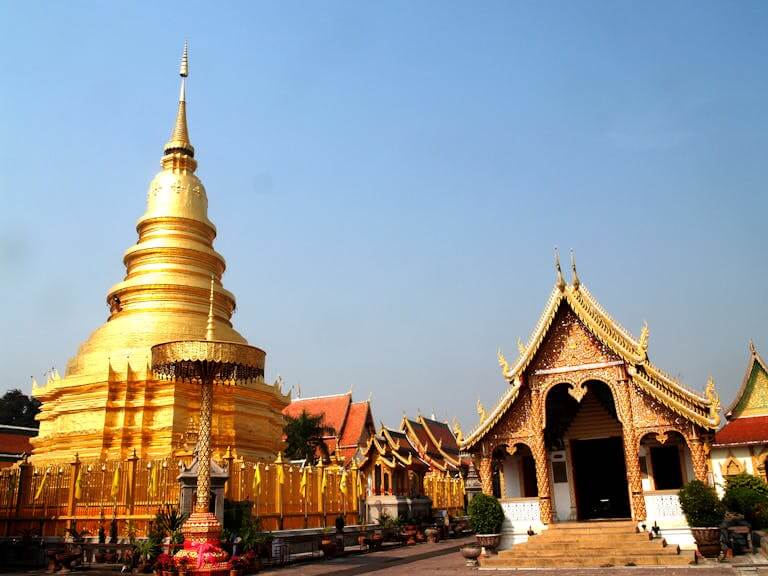 A stunning golden Buddhist temple in Thailand with traditional architecture under a clear blue sky.