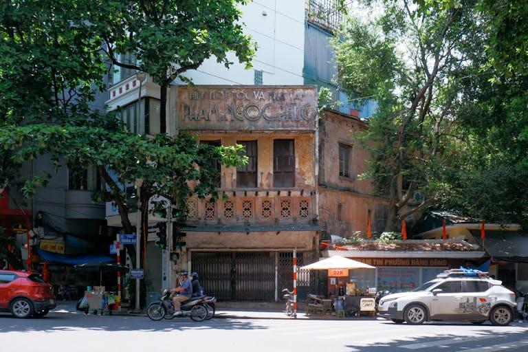 Street view of a historic building in Hà Nội, Vietnam, with passing traffic and vibrant urban life.