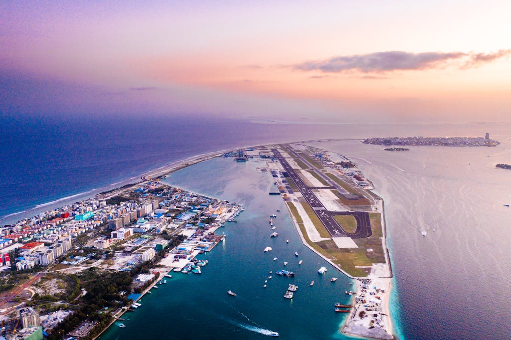 A breathtaking aerial view of a coastal city and airport at sunset with vibrant hues, capturing the blend of urban and natural beauty.